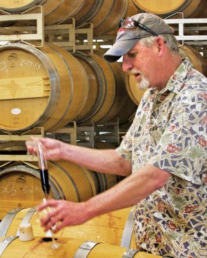 At top: Harvest time at the Holy Cross vineyard. Photo courtesy of the Winery. Above: Winemaker Matt Cookson siphons a gold medal Merlot from an oak barrel for sampling. Photo by Padgett McFeely.