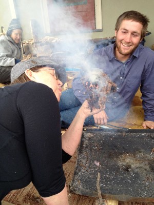 Opposite page:  Sam Liebl looks on as Teresa Koransky blows a tinder bundle into flame – the last step of making a friction fire.
