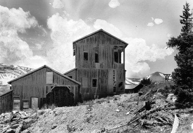 This view of the abandoned silver mill near, Leavick, Park County, Colorado, shows dilapidated wood mining structures and remains of the 13,000-foot tramway framework that brought down ores from the Last Chance lode and the Hilltop mines. Mount Sheridan (13,748 feet) and the glacier-formed Horseshoe Cirque are in the distance. Photo was taken between 1940 and 1950. Courtesy of the Denver Public Library