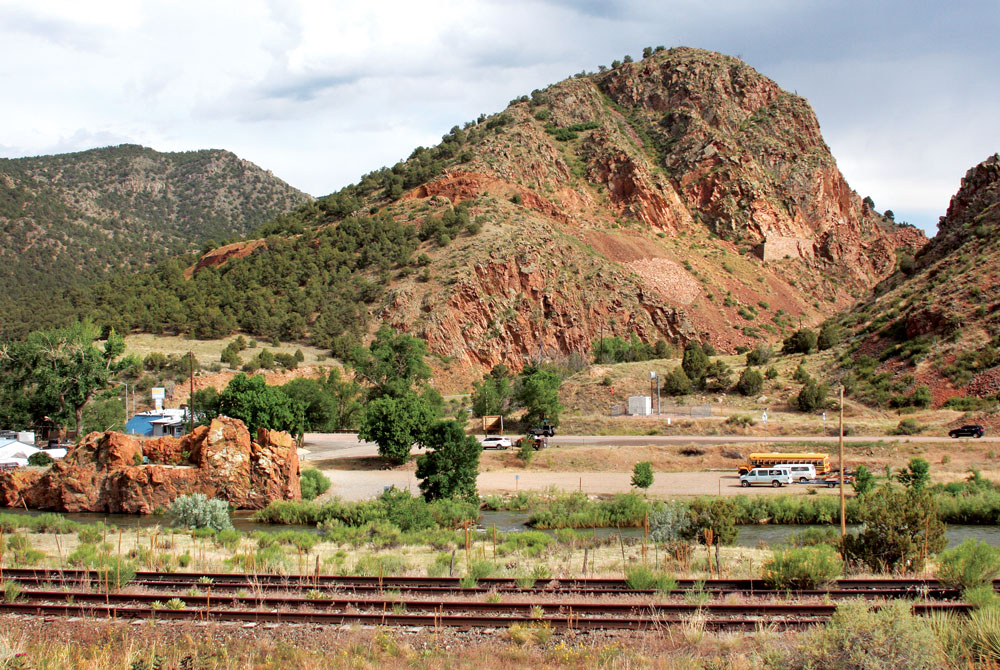 The same view today shows the Arkansas River and U.S. Highway 50. A stone retaining wall is still visible on the hillside. The red rock formation on the left was once used to help support the railroad bridge.  Photo by Mike Rosso.
