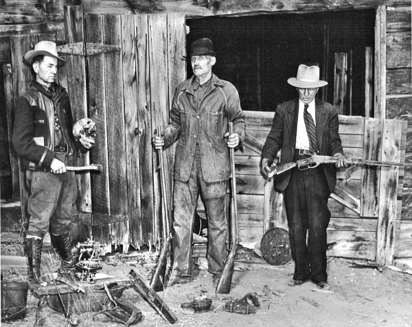 The photo above was taken at Gottlieb Fluhmann’s cabin near Lake George soon after his remains were found in a hidden cave. Left to right are Fairplay Flume writer Everett Bair holding Fluhmann’s skull, Dan Denny with Fluhmann’s flintlock rifles, and Sheriff Law holding the bullet-damaged rifle. Courtesy, Randy and Brenda Myers of Mule Creek Outfitters, Lake George, Co.